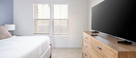 A bedroom with a bed, a dresser, a TV, and a window with blinds.