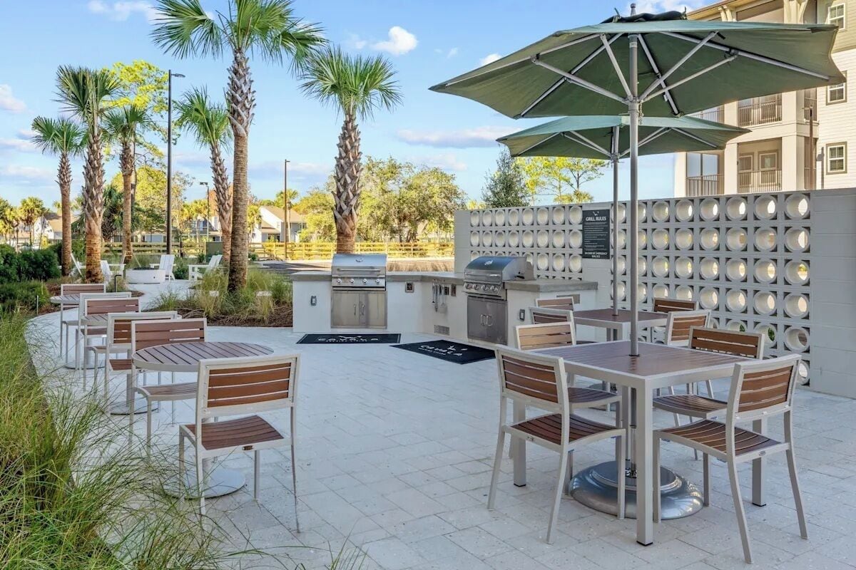 Een terras buiten met tafels en stoelen, een barbecue en palmbomen.
