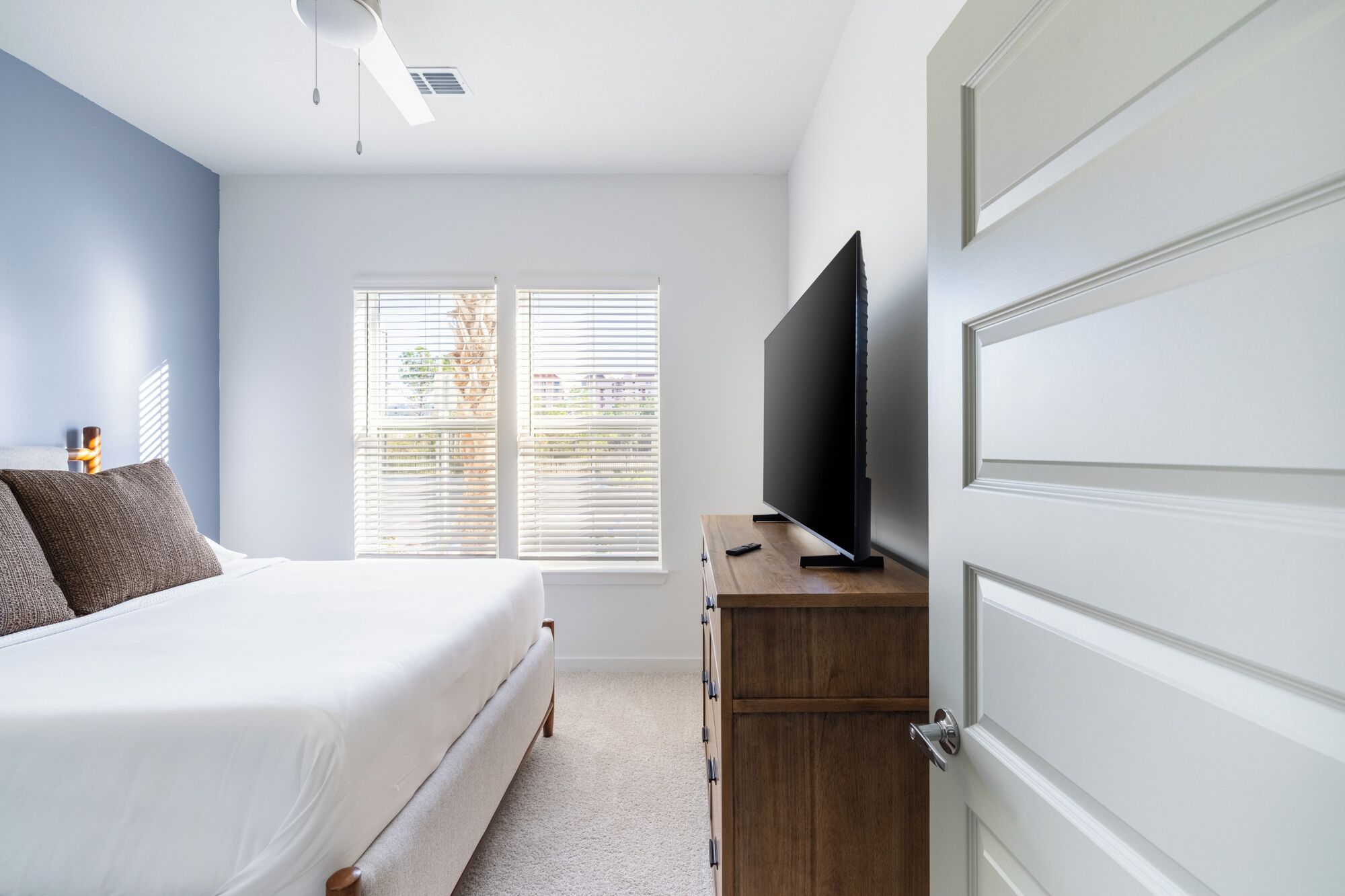 A bedroom with a bed, a TV on a wooden stand, and a wardrobe.