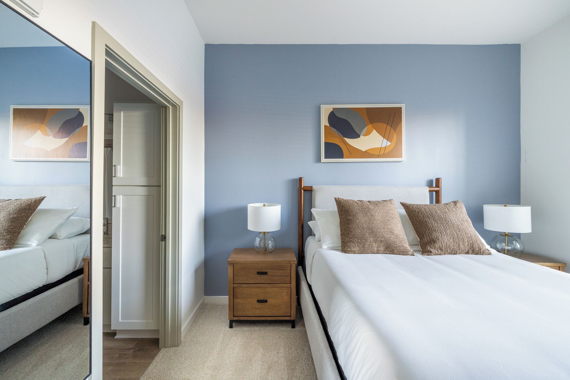 Een slaapkamer met een bed, nachtkastjes, een spiegel en abstracte kunst aan de wanden.
