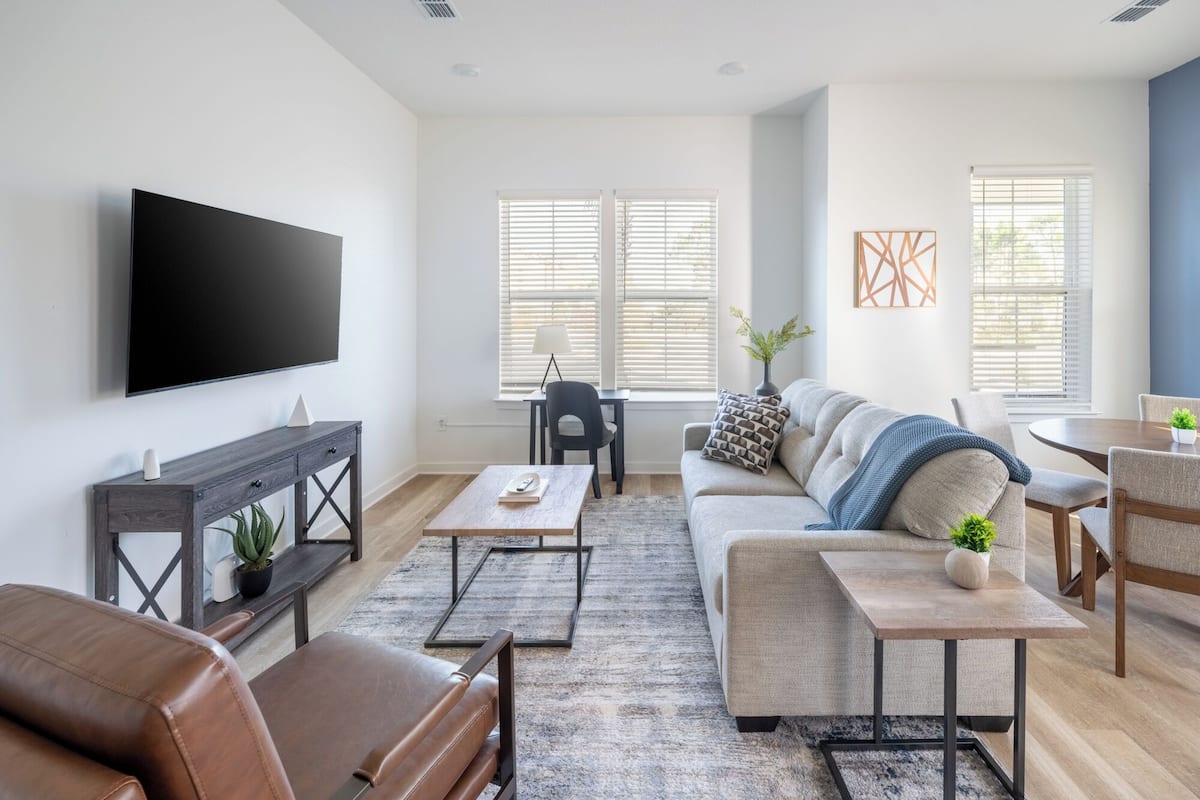 A modern living room with a flat-screen TV, leather sofa, coffee table, and a dining area with a table and chairs.