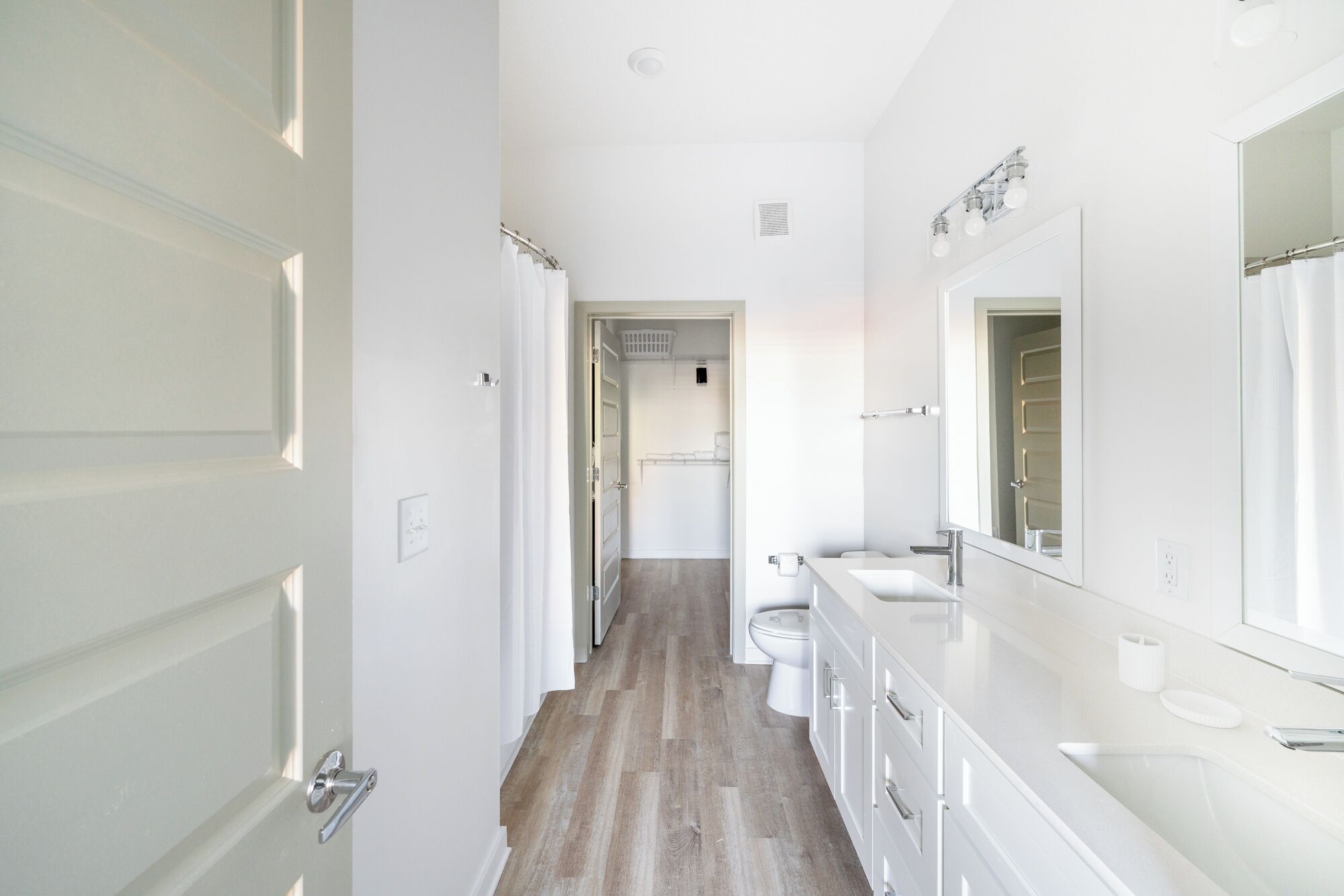 A modern bathroom with a large mirror, white fixtures, and a wooden floor.