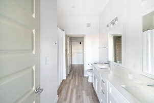 A modern bathroom with a large mirror, white fixtures, and a wooden floor.