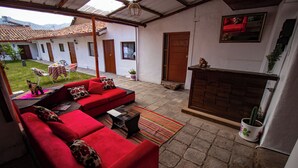 A red sofa set with a small table and a rug in a covered outdoor area with a fireplace and a potted plant. - Encanto San Blas (Cusco)