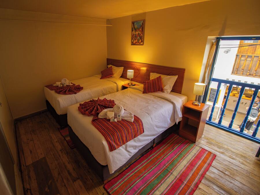 Habitación de hotel con dos camas, piso de madera, alfombra a rayas de colores y un cuadro en la pared.