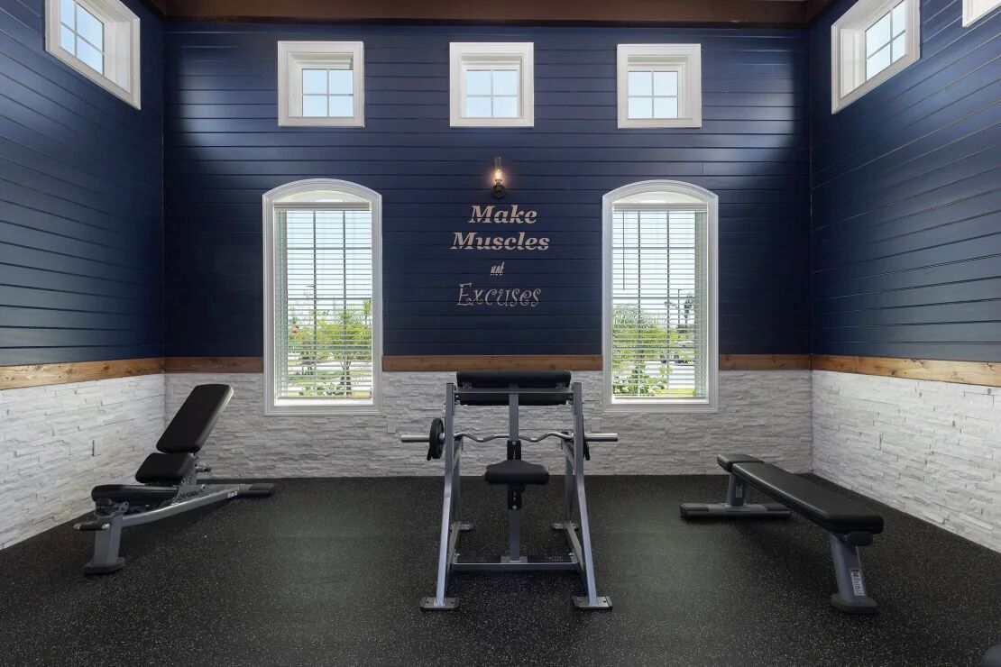 Un gimnasio con una frase motivacional en la pared, equipamiento de ejercicio y ventanas amplias.