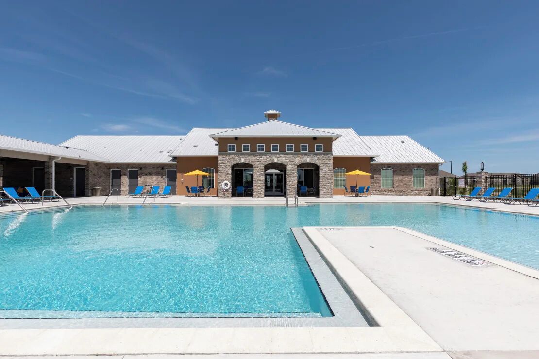 Una piscina con acqua azzurra, circondata da sdraio e un edificio con facciata in pietra e tetto in metallo.