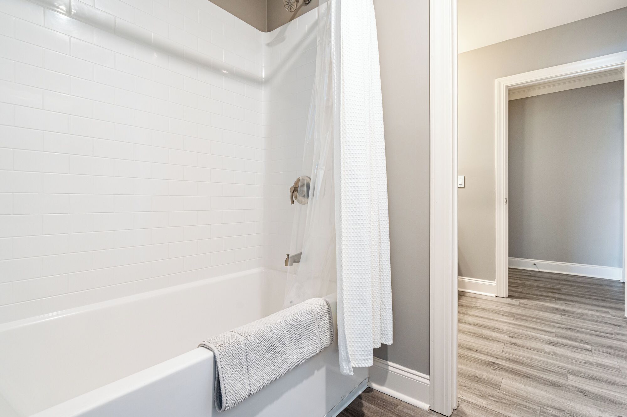 A bathroom with white tiled walls, a bathtub, and a shower curtain.