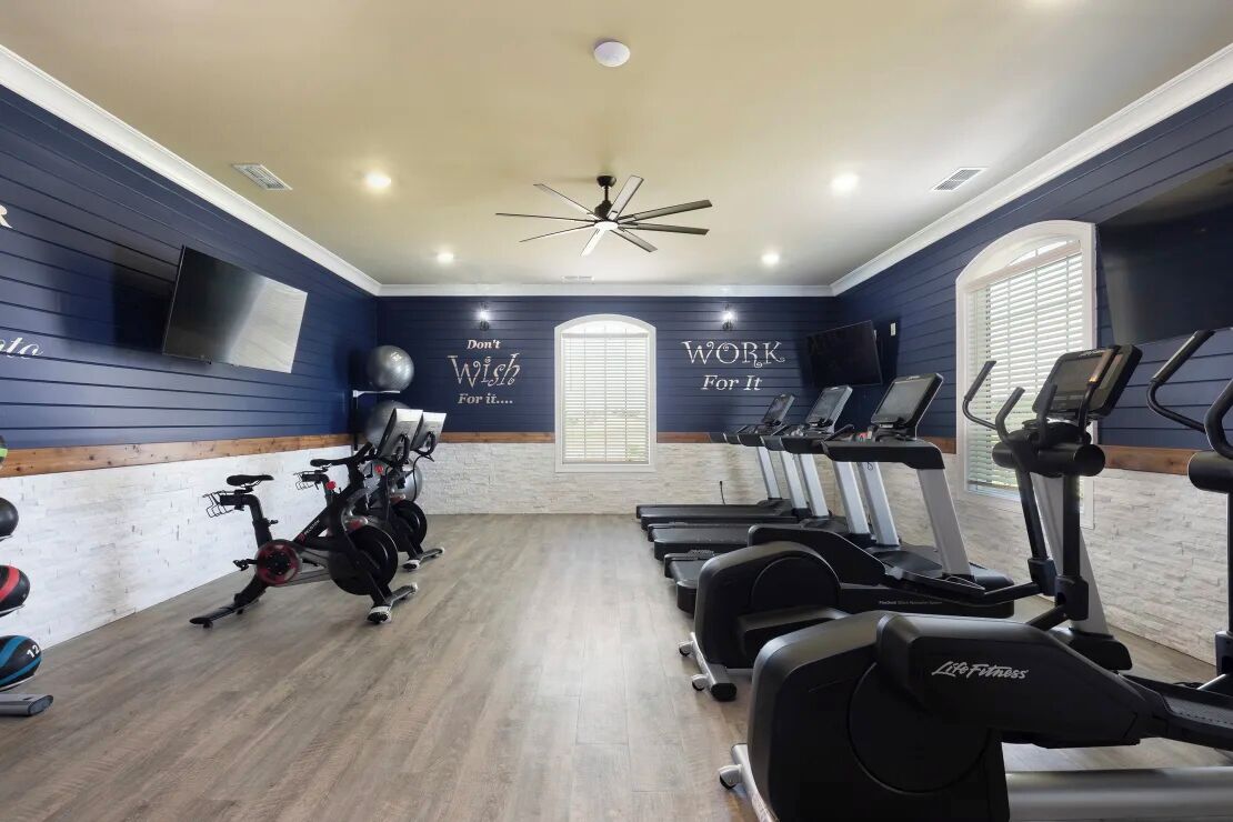 Une salle de sport équipée de matériel d’exercice, ornée de citations inspirantes sur les murs et dotée d’un ventilateur au plafond.
