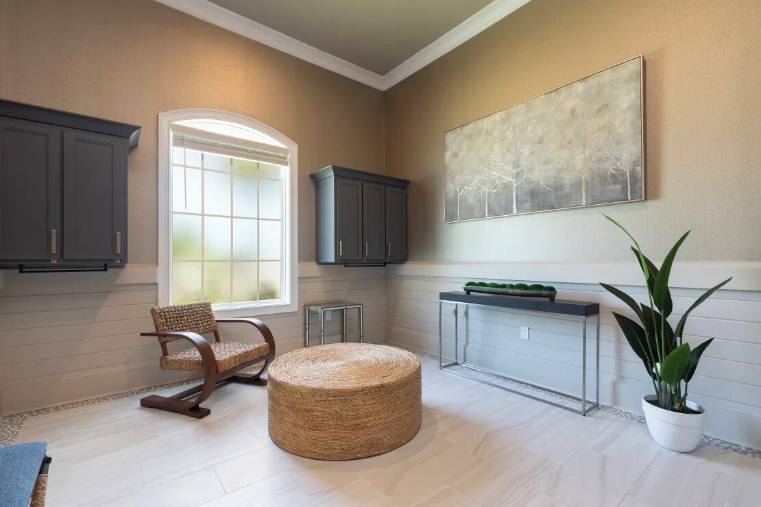 Une cuisine moderne avec une grande fenêtre, des meubles de couleur sombre, un pouf rond en osier et une plante en pot.