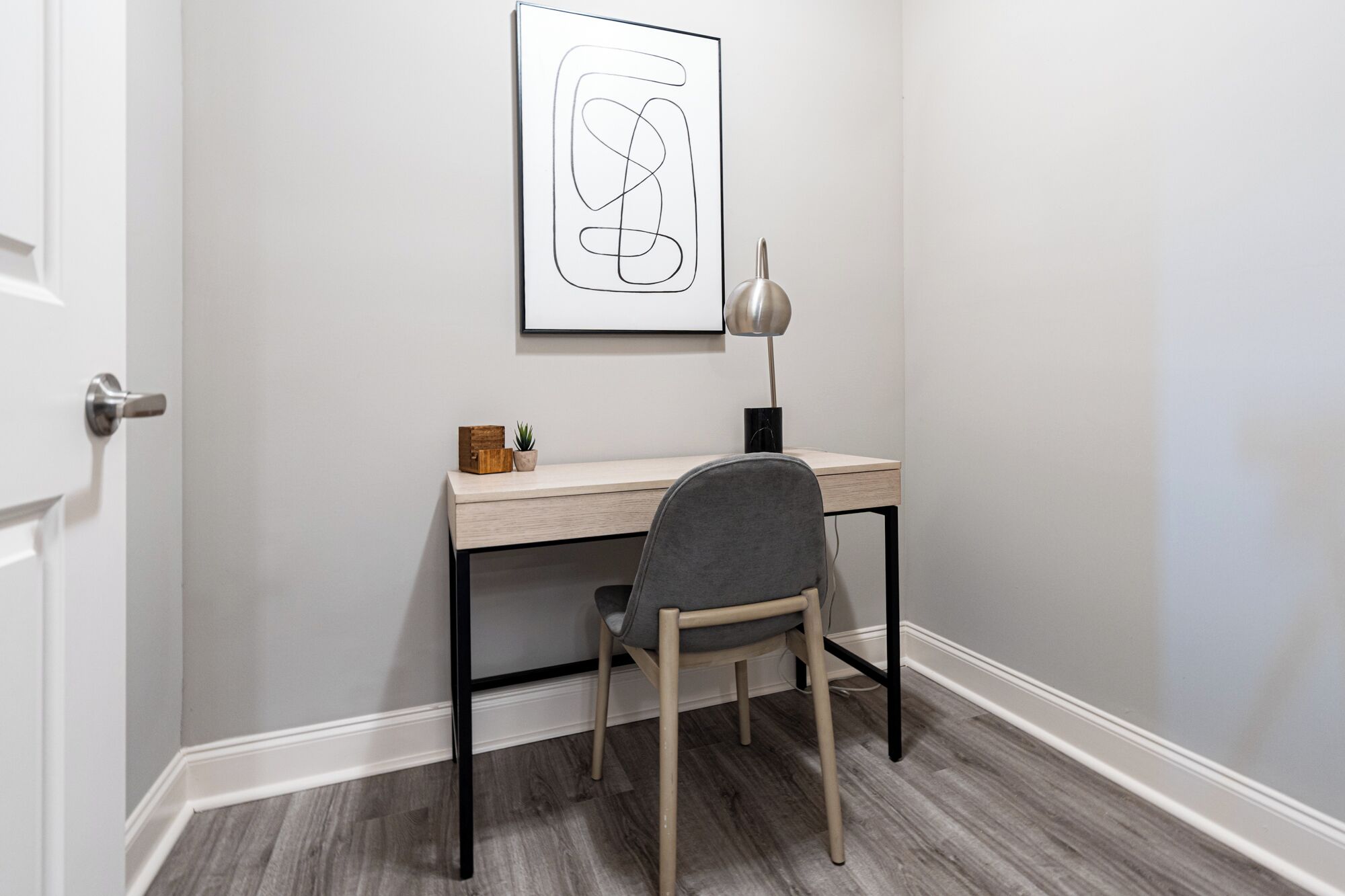 Un espacio de oficina pequeño y ordenado con un escritorio, una silla y una obra de arte abstracta enmarcada en la pared.