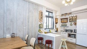 A modern kitchen with a wooden dining table, two bar stools, and a central island. - GREEN LANE B&B (Hualien)