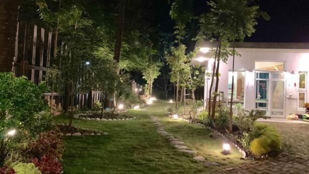Ein Gartenpfad bei Nacht, der zu einem Gebäude mit Glastür führt, umgeben von Bäumen und beleuchtet durch Bodenleuchten.