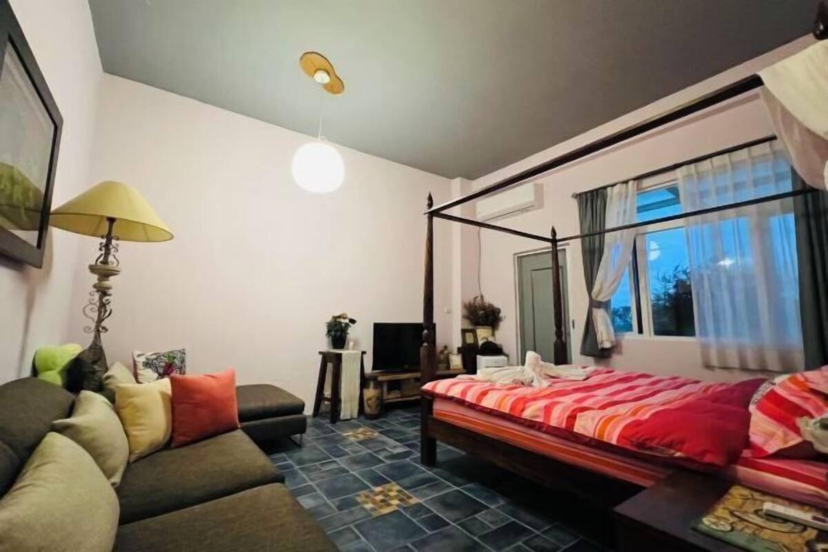 Een slaapkamer met een hemelbed, een bank, een televisie en een raam met gordijnen.