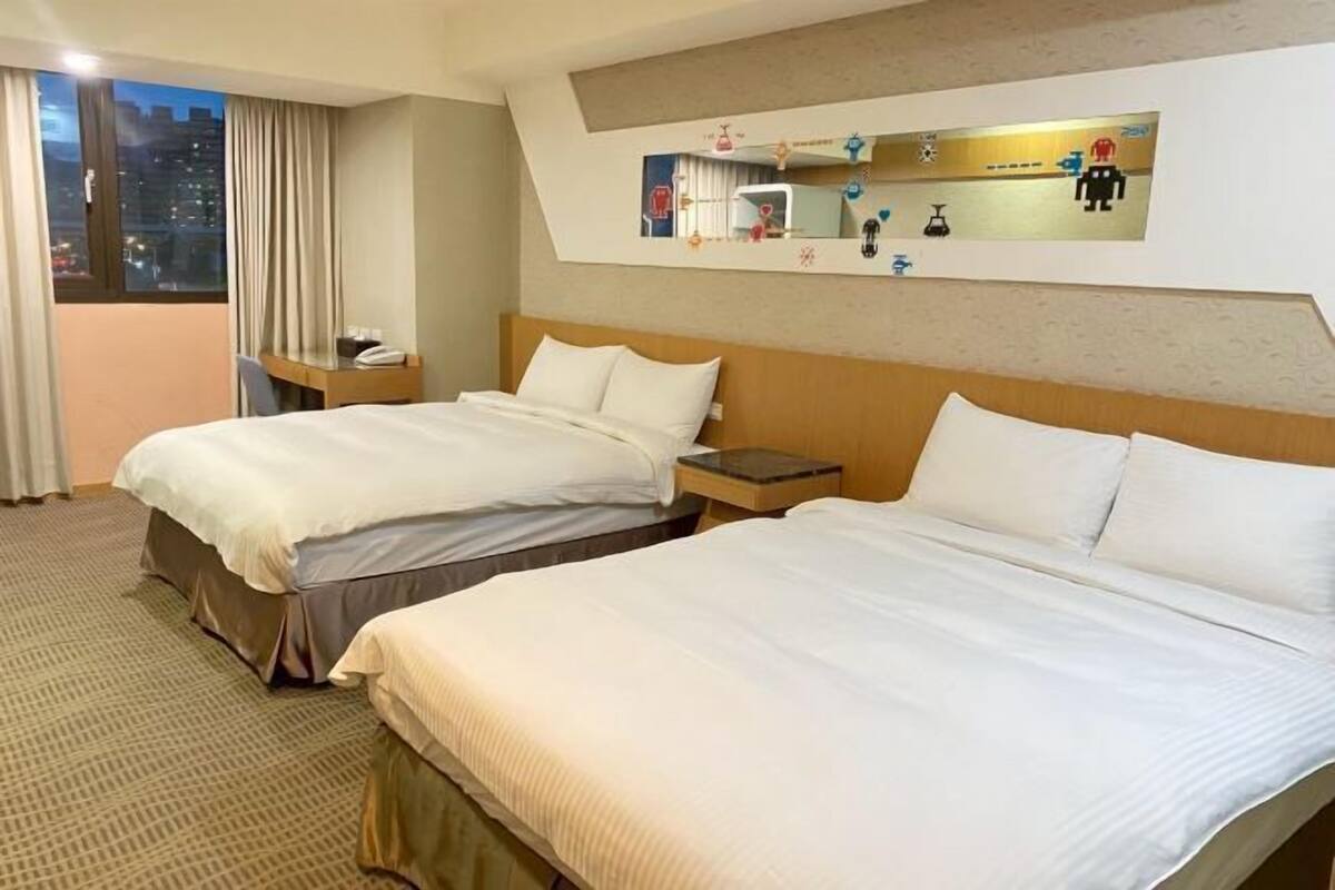 A hotel room with two beds, a desk, a chair, a nightstand, and a large mirror.