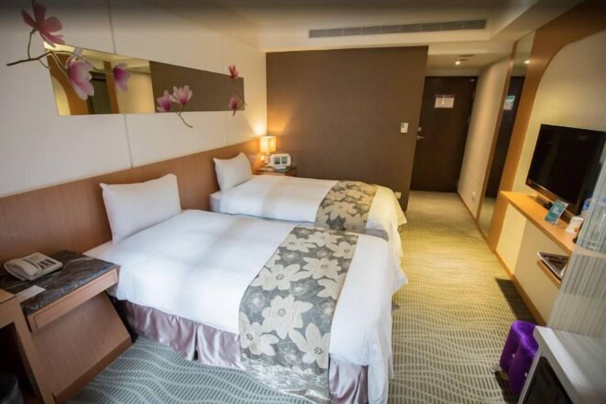 A hotel room with two beds, a TV, a desk with a phone, and a mirror.