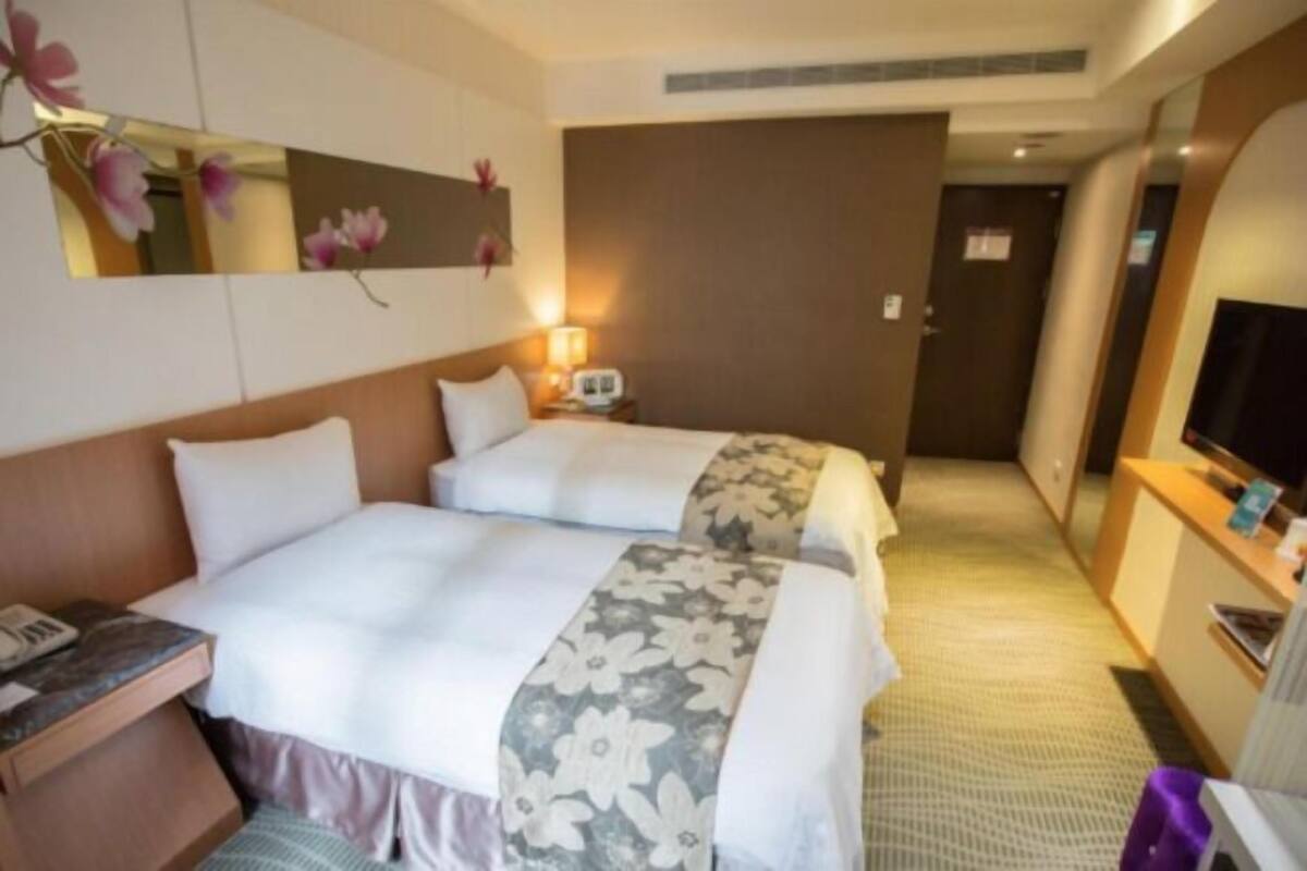 A hotel room with two beds, a TV, a desk, and a mirror.