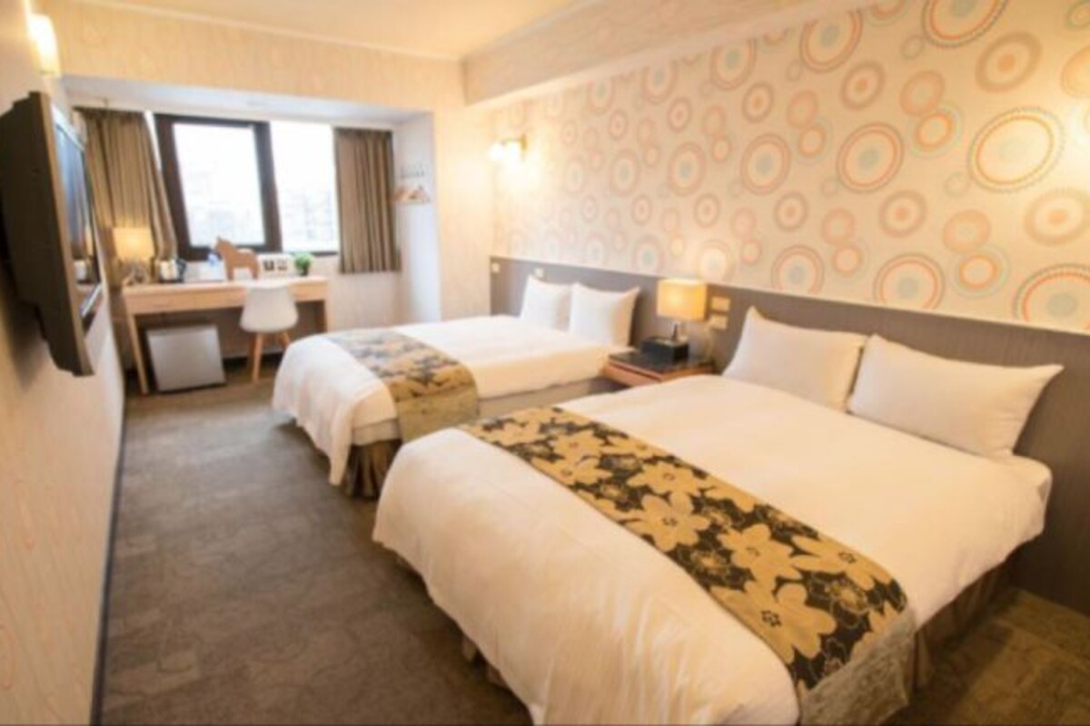 Une chambre d’hôtel avec deux lits, un bureau, une télévision et un mur décoré de motifs.