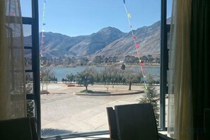 A view through a window with a mountain landscape, a lake, and a paved area with trees and benches. - CHP. Hotel (Heqing)