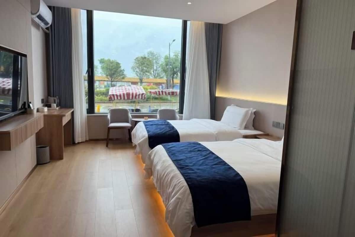 Une chambre d’hôtel avec deux lits, un bureau, une chaise et une grande fenêtre donnant sur l’extérieur.