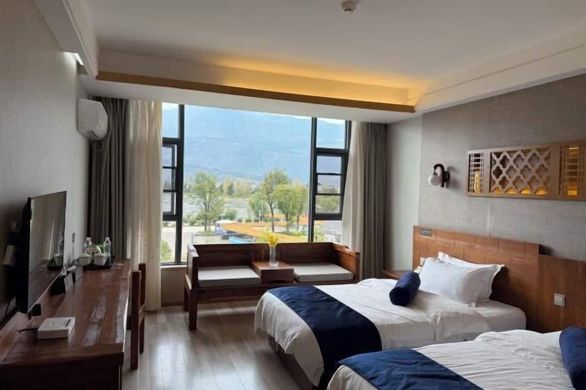 Une chambre d’hôtel avec deux lits, une télévision, un bureau et une grande fenêtre donnant sur des arbres et des montagnes.