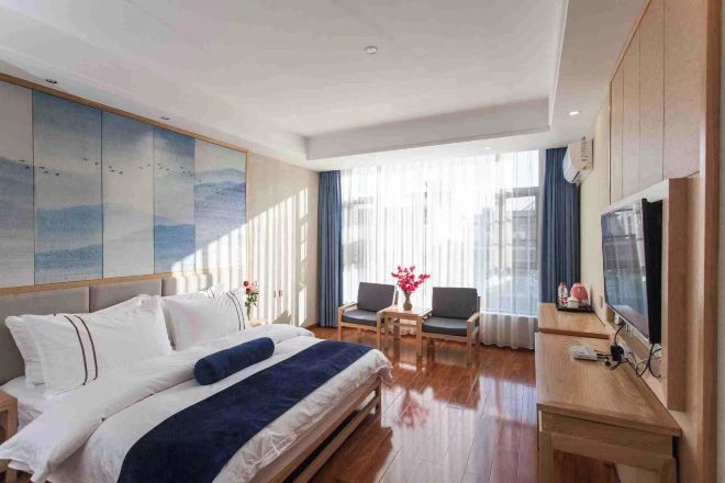 Habitación de hotel con cama, escritorio, silla, televisión y un amplio ventanal con cortinas.