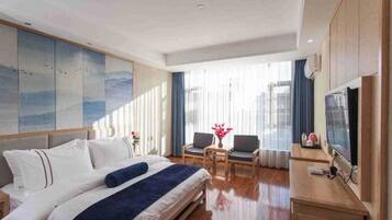Habitación de hotel con cama, escritorio, silla, televisión y un amplio ventanal con cortinas.