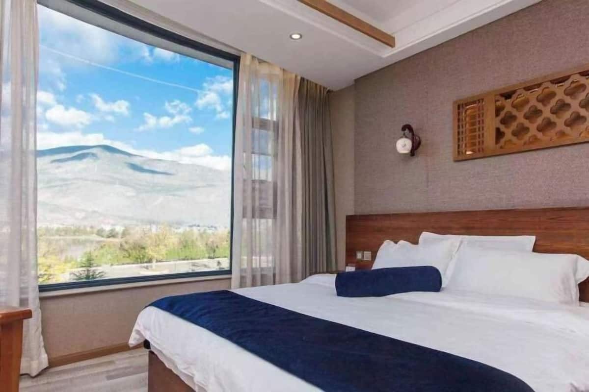 Une chambre d’hôtel dotée d’une grande fenêtre donnant sur les montagnes, d’une tête de lit en bois et d’un panneau décoratif mural.
