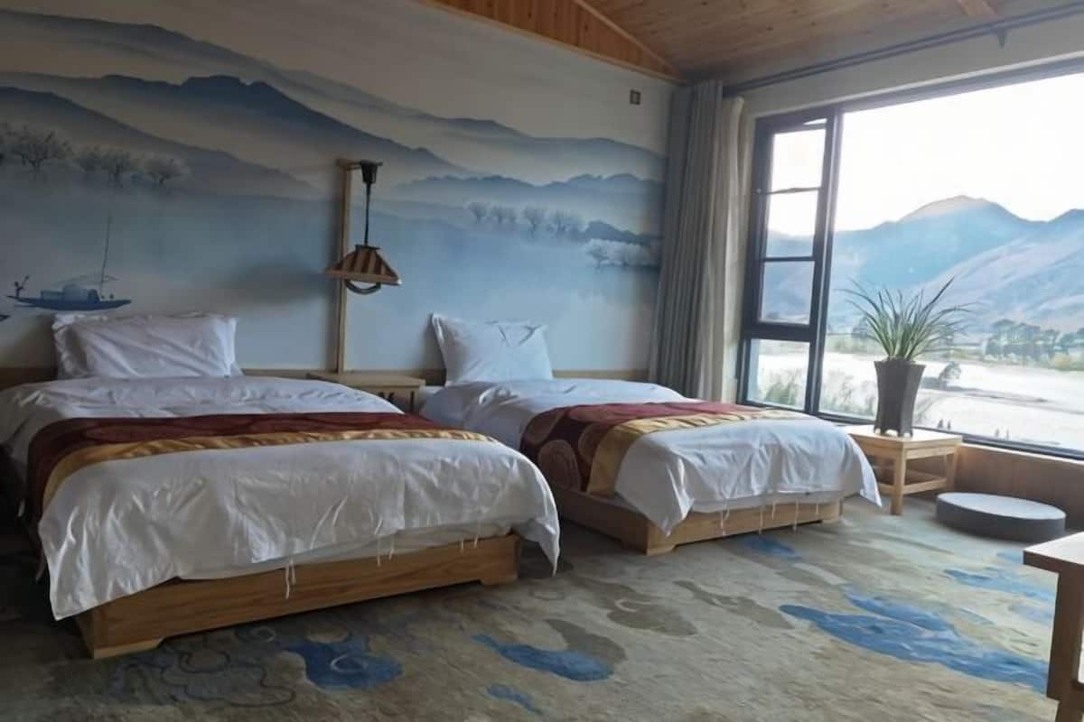Une chambre avec deux lits, une grande fenêtre, une fresque murale et une plante en pot.
