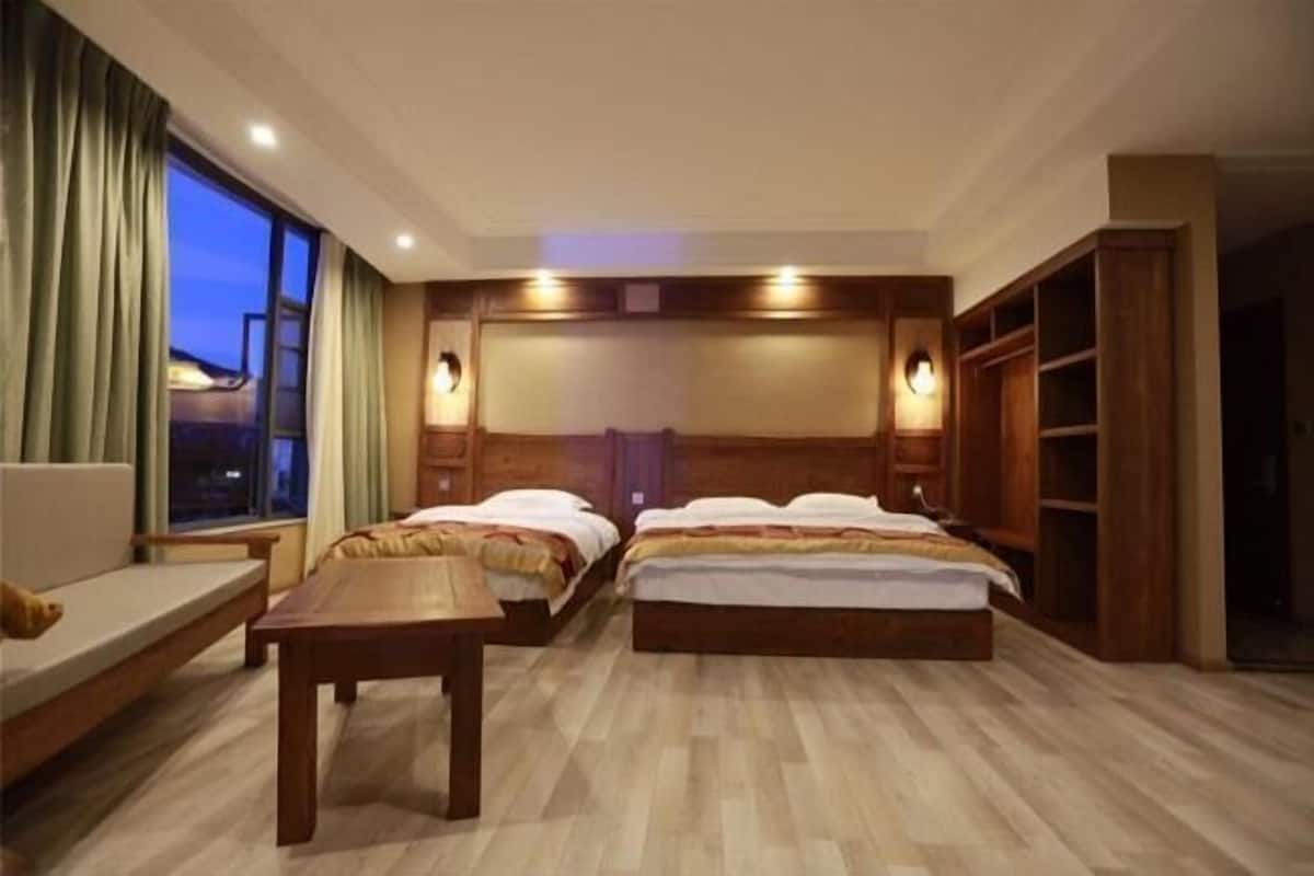 Une chambre d’hôtel avec deux lits, une table en bois, un canapé et une grande fenêtre.