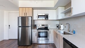 A modern kitchen with stainless steel appliances, white cabinetry, and a wooden floor.
