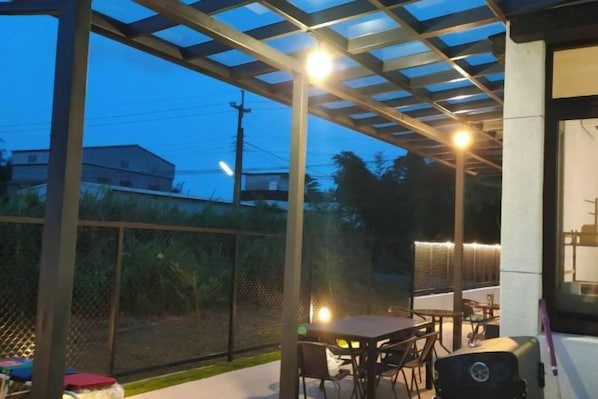An outdoor patio with tables and chairs, a grill, and a pergola structure.