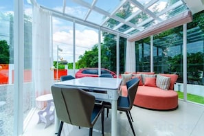 A modern indoor space with a glass ceiling, a dining table with chairs, and a red sofa.