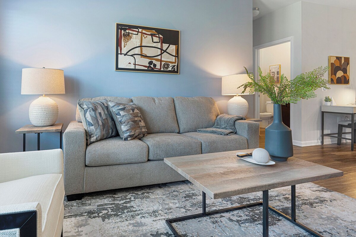 Un salon moderne avec un canapé gris, une table basse et une lampe.