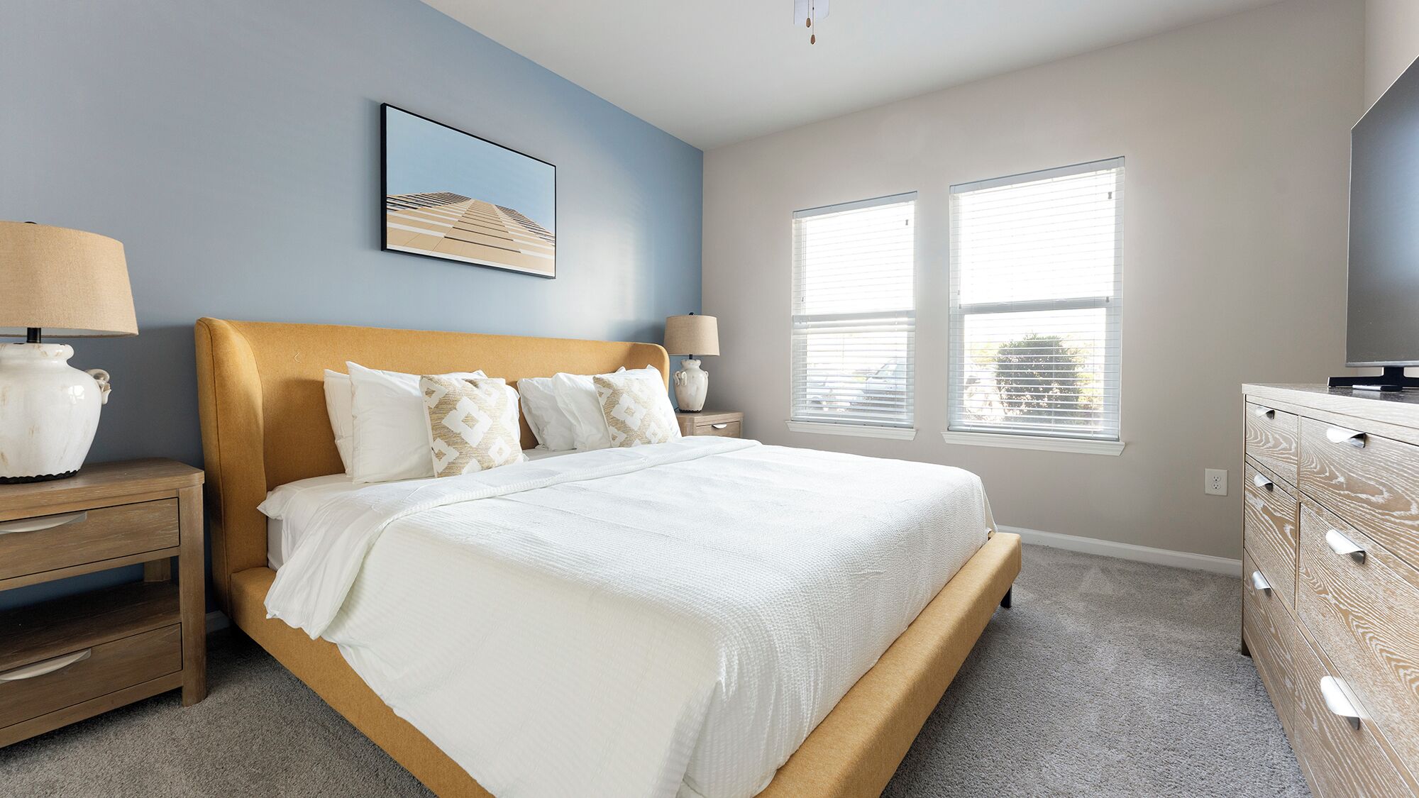 A bedroom with a bed, nightstands, a dresser, and a window with blinds.