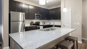 A modern kitchen with dark cabinets, stainless steel appliances, a granite countertop, and a built-in sink. - Carolina Forest Furnished Apartments by Landing  (Myrtle Beach)