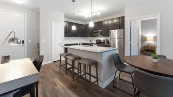 A modern kitchen with dark cabinets, stainless steel appliances, a central island with stools, and a dining area with a table and chairs.
