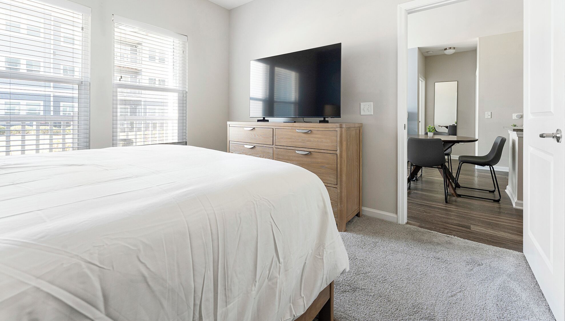 Een slaapkamer met een groot bed, een televisie op een houten dressoir en uitzicht op de stad door het raam.