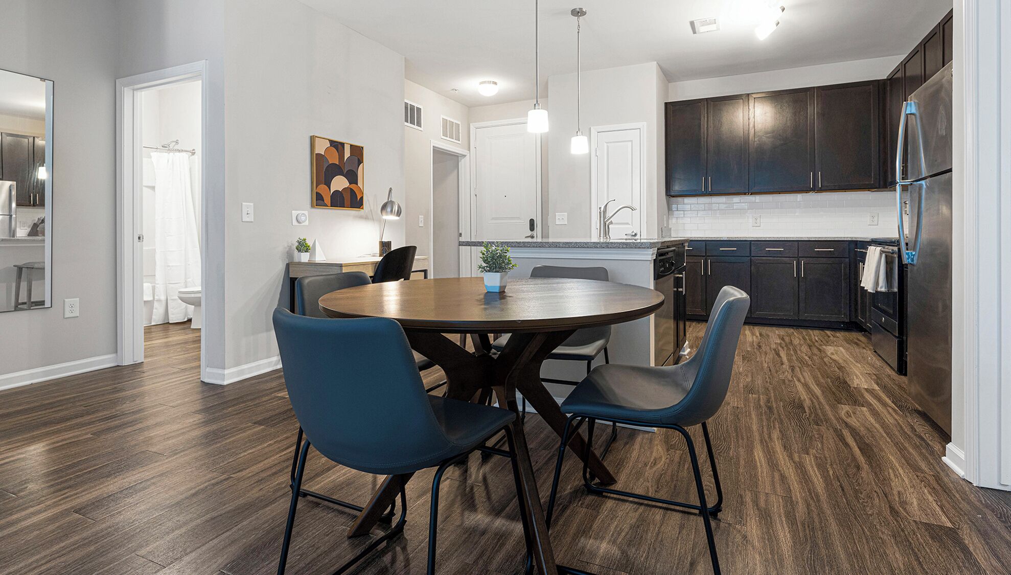 Een moderne keuken met donkere kastjes, een roestvrijstalen koelkast en een eethoek met een ronde tafel en blauwe stoelen.