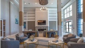 A spacious living room with a fireplace, comfortable seating, and a large window providing natural light. - Carolina Forest Furnished Apartments by Landing  (Myrtle Beach)