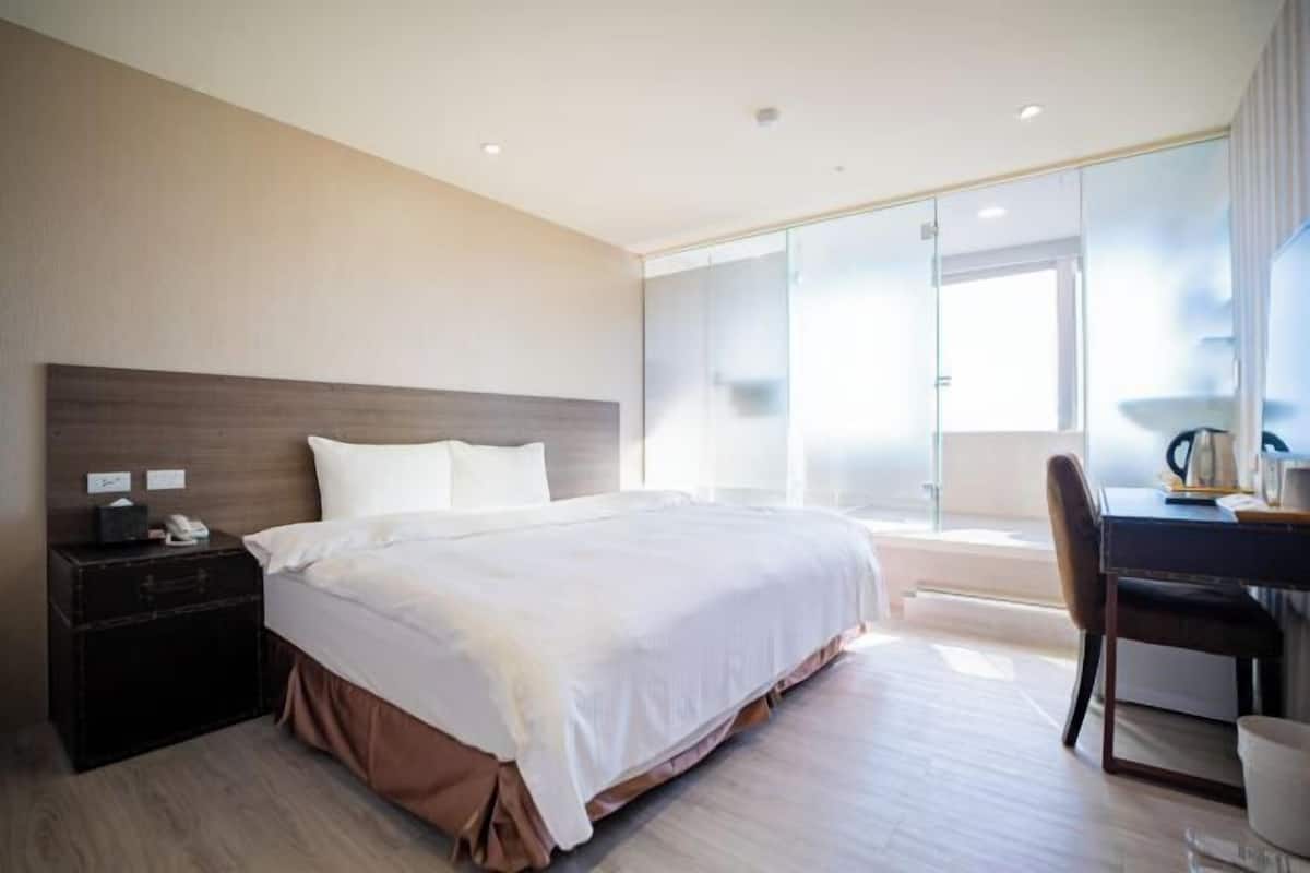 Moderni hotellihuone, jossa on suuri sänky, työpöytä ja lasiliukuovi, joka johtaa parvekkeelle.