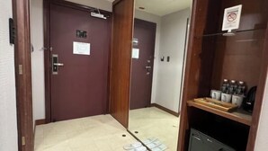 Une chambre d’hôtel avec une porte en bois, une petite étagère avec des articles de toilette et un sol carrelé.