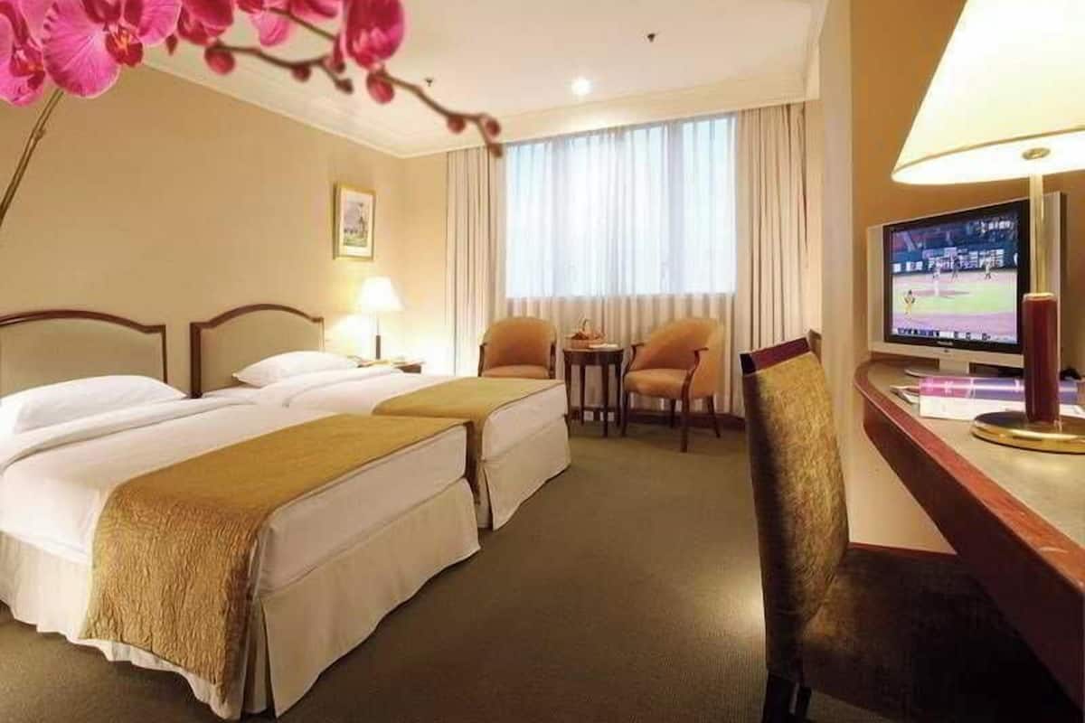 Hotellihuone, jossa on kaksi sänkyä, televisio, kirjoituspöytä lampun kanssa ja tuoli.