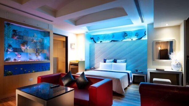 A hotel room with a bed, a desk, a red sofa, and a large aquarium. - Only Love Motel (New Taipei City)