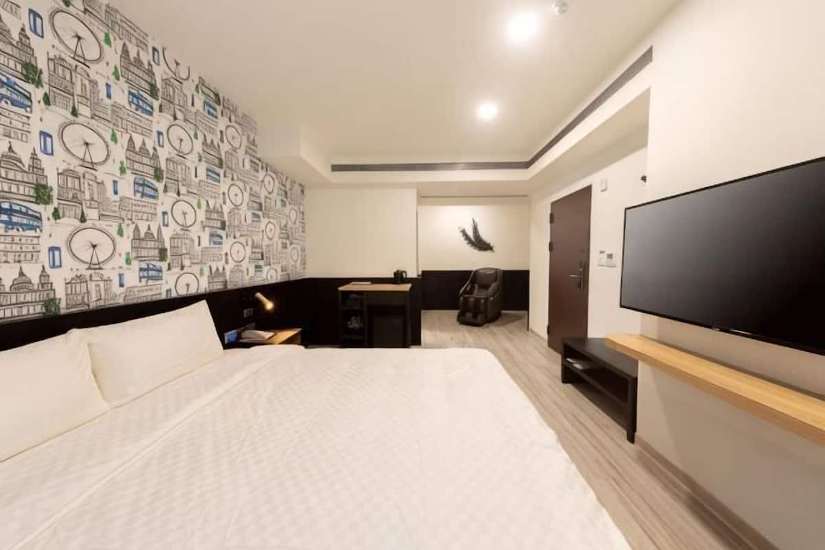 Une chambre d’hôtel avec un grand lit, un téléviseur à écran plat, un mur décoré d’un motif représentant une horloge, et une porte donnant sur une salle de bain.
