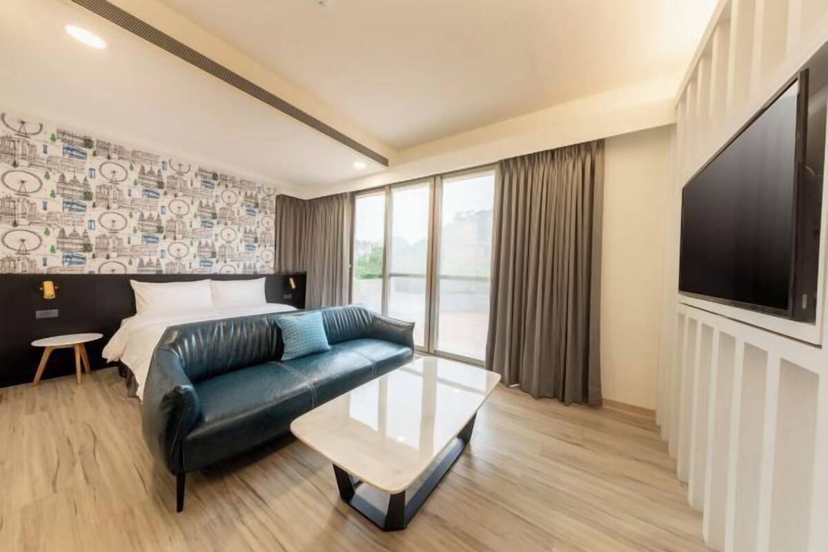 Une chambre d’hôtel moderne avec un canapé en cuir, une table basse en verre, un grand téléviseur et un papier peint à motifs.