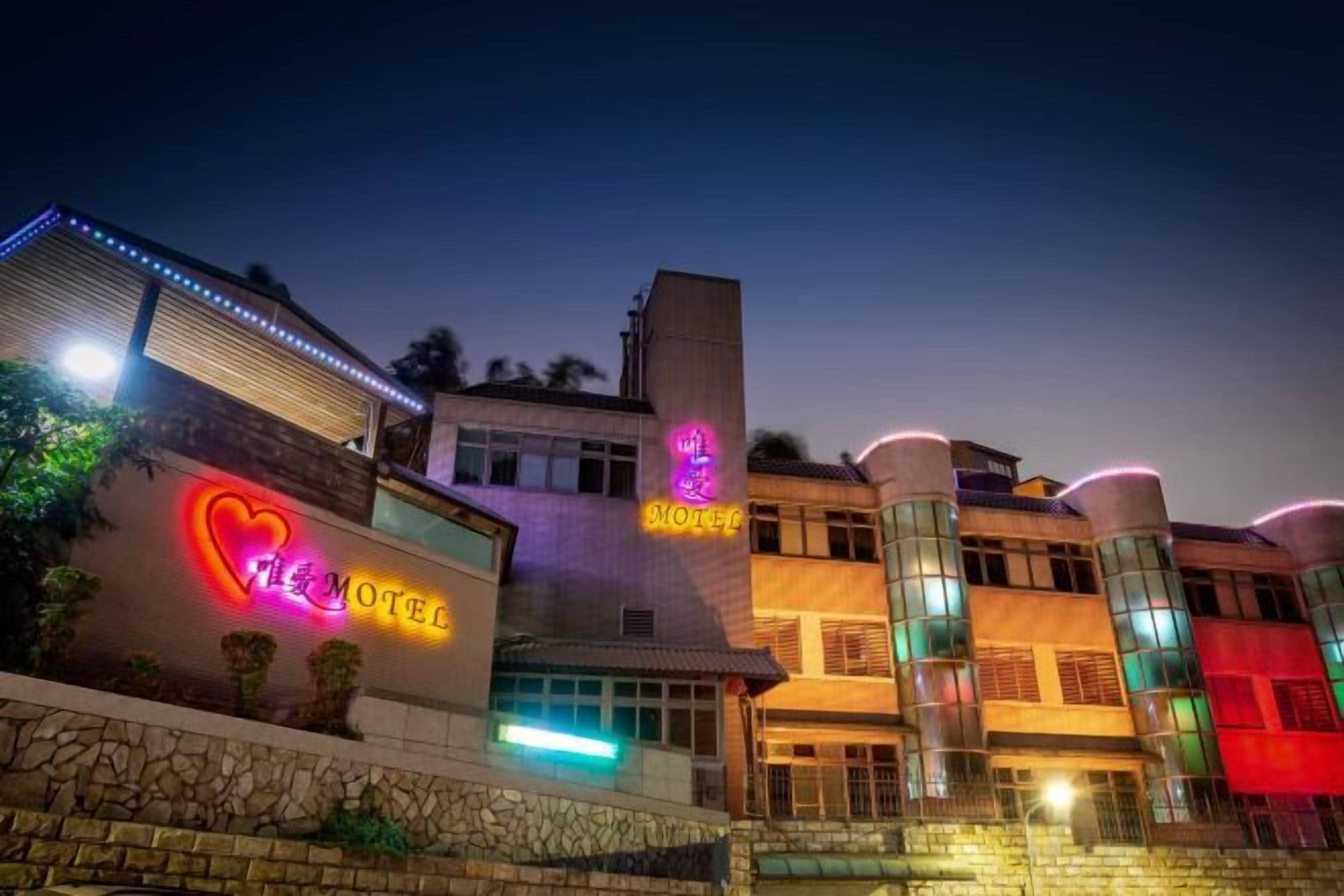 A hotel with a neon sign, a stone facade, and a modern design.