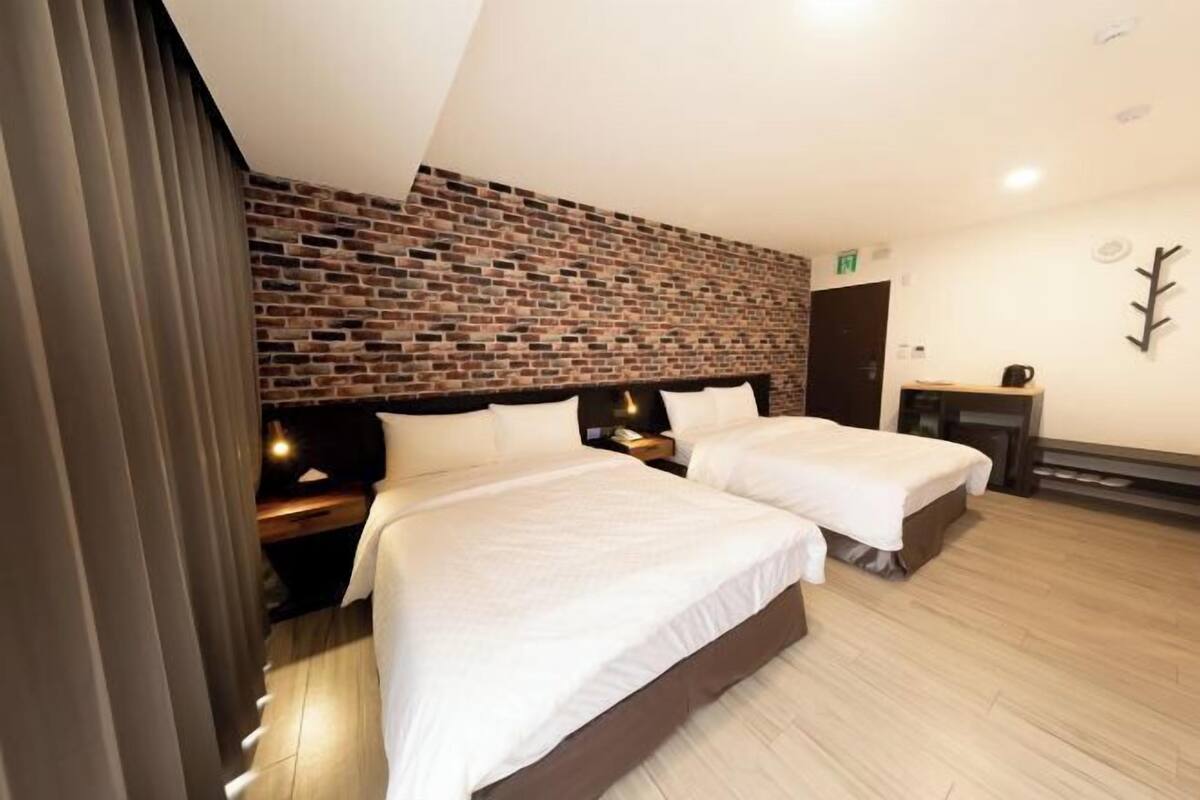 Une chambre d’hôtel avec deux lits, un mur décoratif en briques et un plancher en bois.