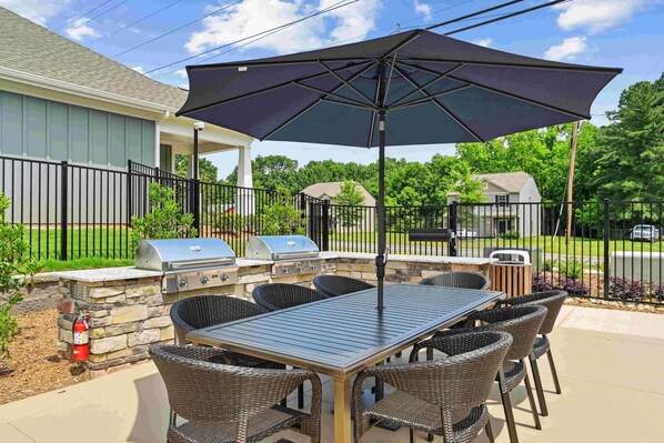 An outdoor patio with a grill, dining table, chairs, and an umbrella. - Newell Furnished Apartments by Landing (Charlotte)