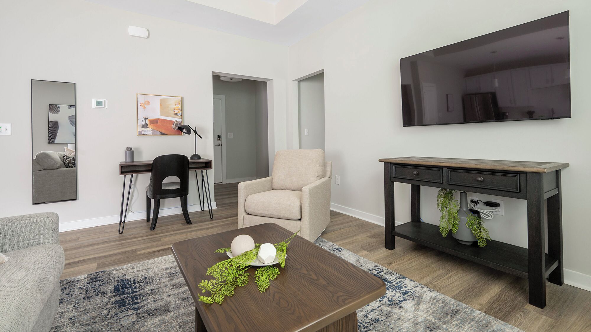 Una sala de estar moderna con un sofá, una mesa de centro, un televisor, un escritorio con una silla y una consola con una planta.